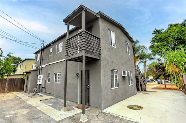 rear view of property with stucco siding, fence, stairway, a balcony, and a patio area