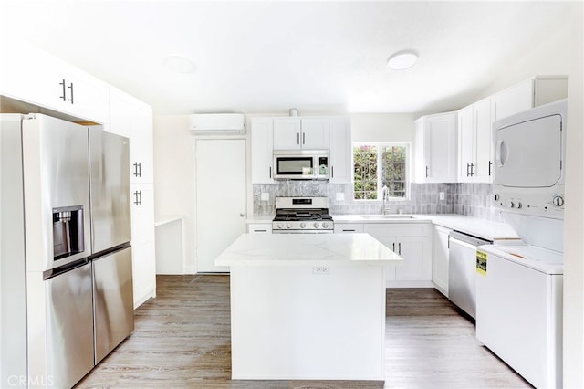 kitchen featuring appliances with stainless steel finishes, sink, a kitchen island, white cabinetry, and stacked washer and dryer