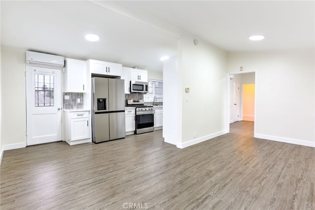 kitchen with appliances with stainless steel finishes, white cabinets, an AC wall unit, and light wood-type flooring