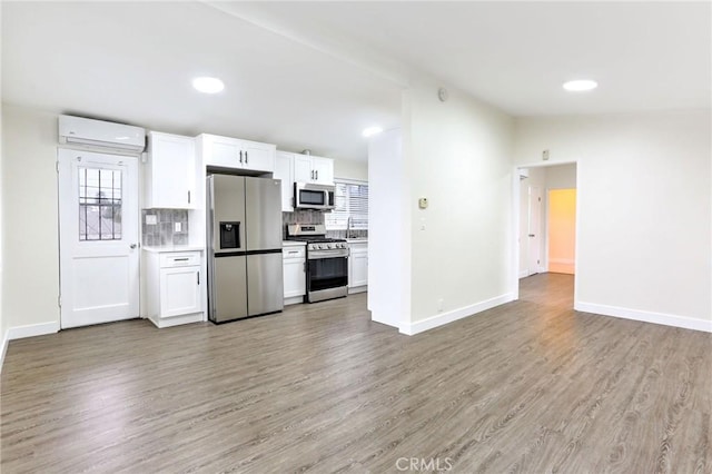 kitchen with stainless steel appliances, a wall mounted air conditioner, white cabinets, baseboards, and light wood-style floors