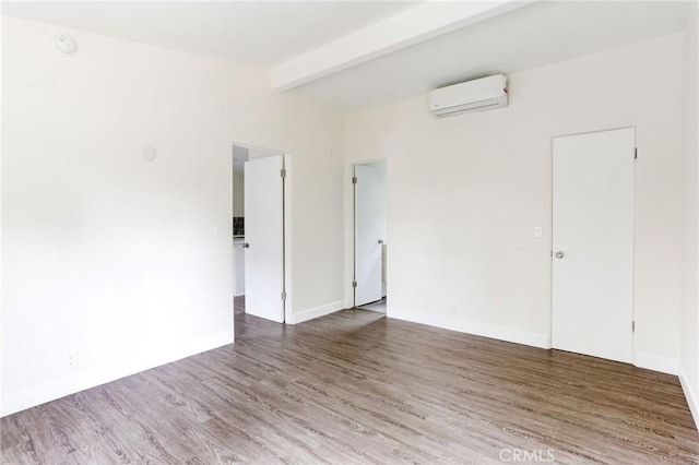 unfurnished room featuring an AC wall unit, baseboards, vaulted ceiling with beams, and wood finished floors