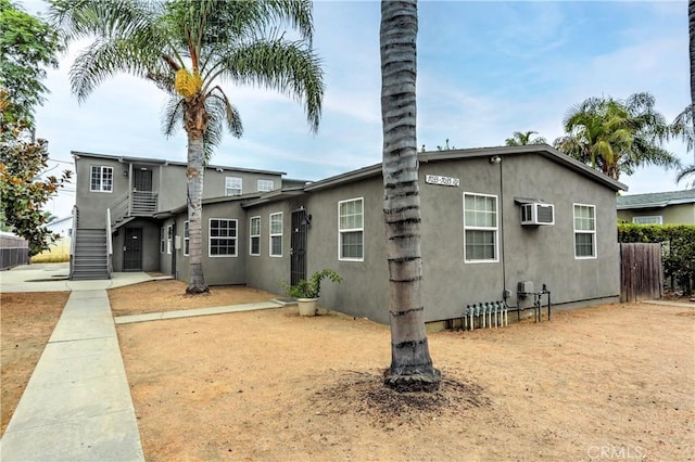 view of front of property with stairs, stucco siding, a wall unit AC, and fence