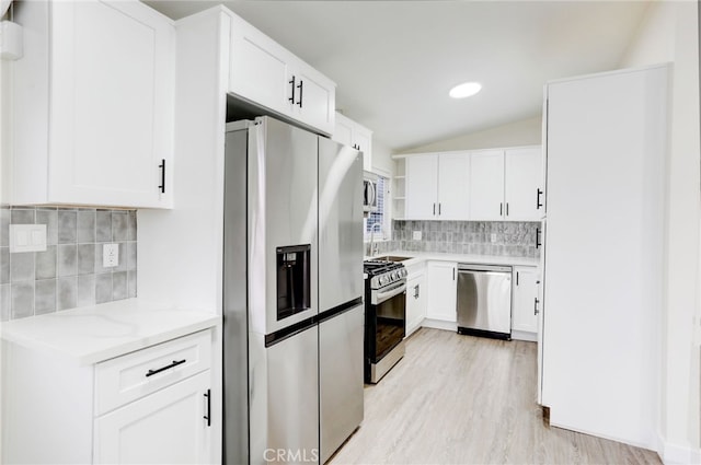 kitchen with appliances with stainless steel finishes, backsplash, white cabinetry, light hardwood / wood-style floors, and vaulted ceiling