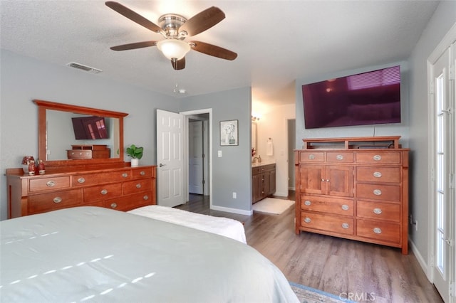 bedroom featuring a textured ceiling, ensuite bath, hardwood / wood-style flooring, and ceiling fan