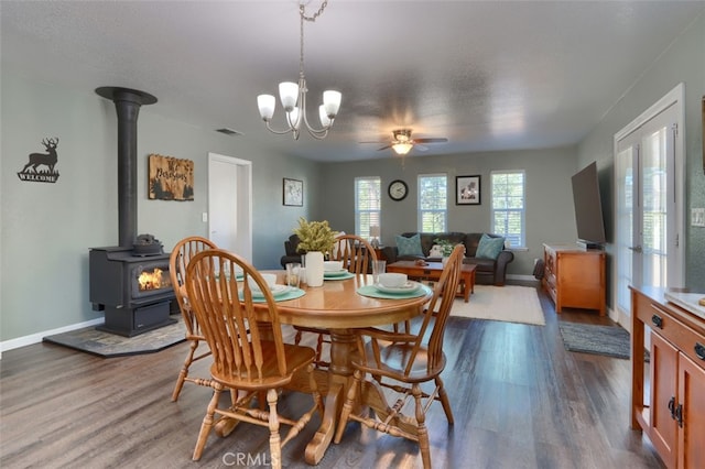 dining area with dark wood-type flooring, ceiling fan with notable chandelier, and a wood stove