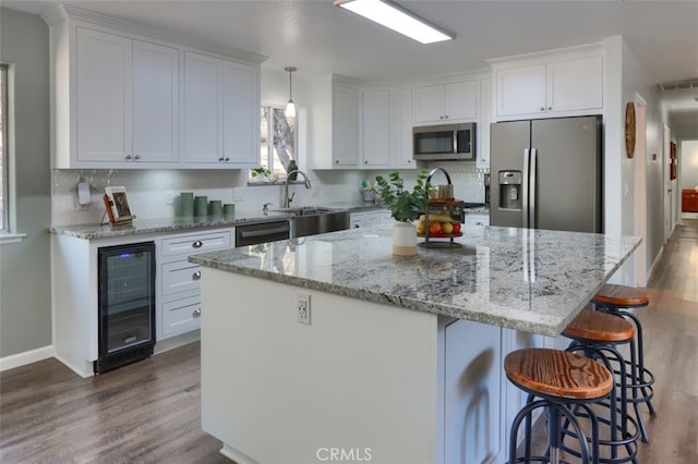 kitchen featuring white cabinets, stainless steel appliances, beverage cooler, and a kitchen island