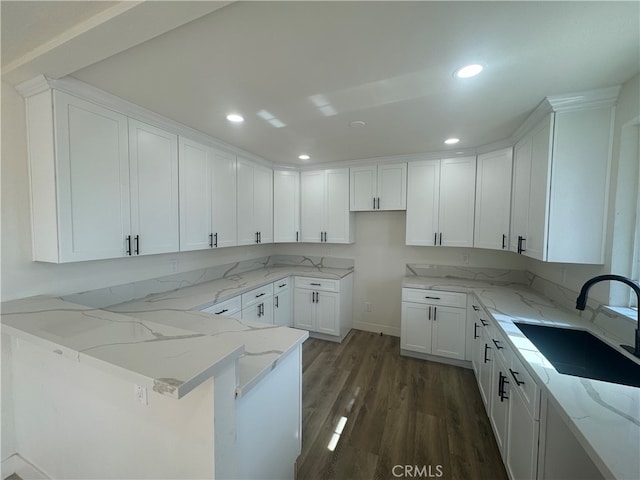 kitchen with kitchen peninsula, white cabinets, light stone countertops, dark hardwood / wood-style floors, and sink