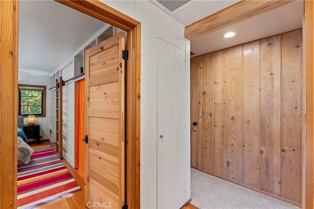 corridor featuring carpet flooring, a barn door, wood walls, and lofted ceiling