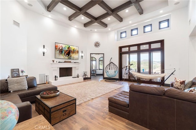 living room with beamed ceiling, a high ceiling, light hardwood / wood-style floors, and coffered ceiling