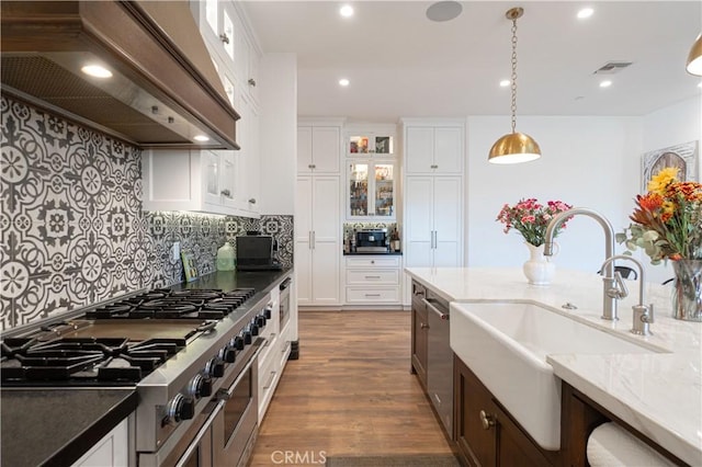 kitchen with sink, dark stone countertops, decorative light fixtures, white cabinets, and custom range hood