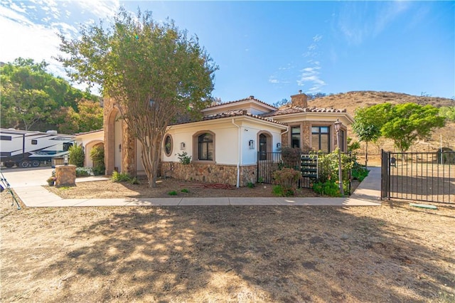 mediterranean / spanish-style house with a chimney, a gate, fence private yard, and stucco siding