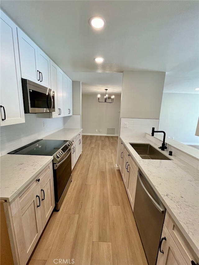 kitchen featuring white cabinets, light stone countertops, light wood-type flooring, sink, and stainless steel appliances