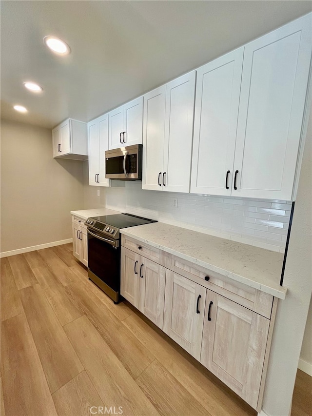 kitchen featuring tasteful backsplash, white cabinetry, stainless steel appliances, light stone counters, and light hardwood / wood-style flooring