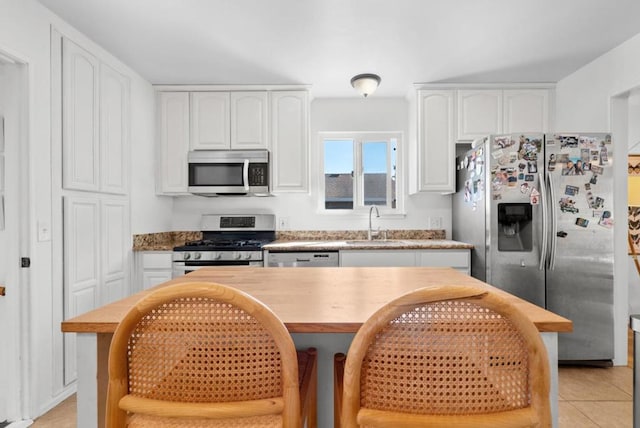 kitchen featuring a breakfast bar, sink, light tile patterned floors, appliances with stainless steel finishes, and white cabinets