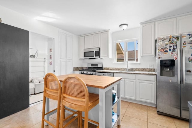 kitchen with light tile patterned flooring, appliances with stainless steel finishes, white cabinetry, wooden counters, and a kitchen breakfast bar