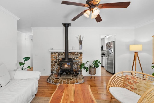 living room featuring light wood-type flooring, ornamental molding, and a wood stove