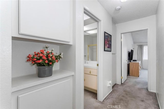 hallway featuring light colored carpet and a textured ceiling