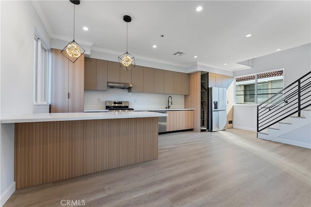 kitchen featuring crown molding, hanging light fixtures, appliances with stainless steel finishes, tasteful backsplash, and light hardwood / wood-style floors