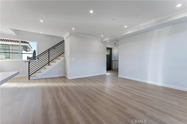 unfurnished living room featuring light wood-type flooring, ornamental molding, and an inviting chandelier