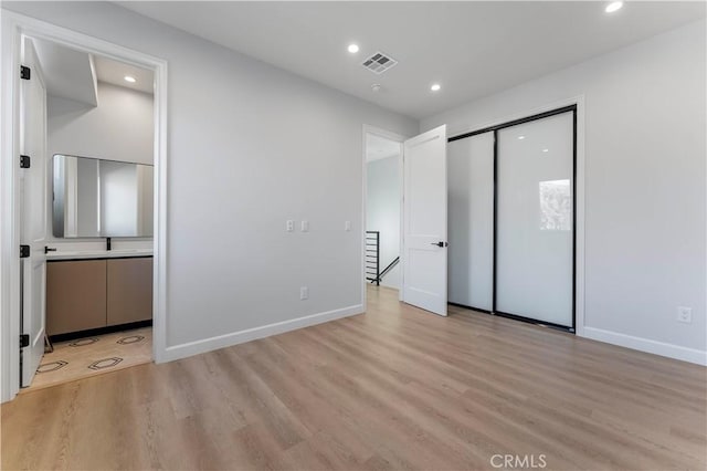 unfurnished bedroom with light wood-type flooring, a closet, and connected bathroom