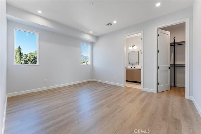 unfurnished bedroom featuring connected bathroom, sink, light hardwood / wood-style floors, and multiple windows