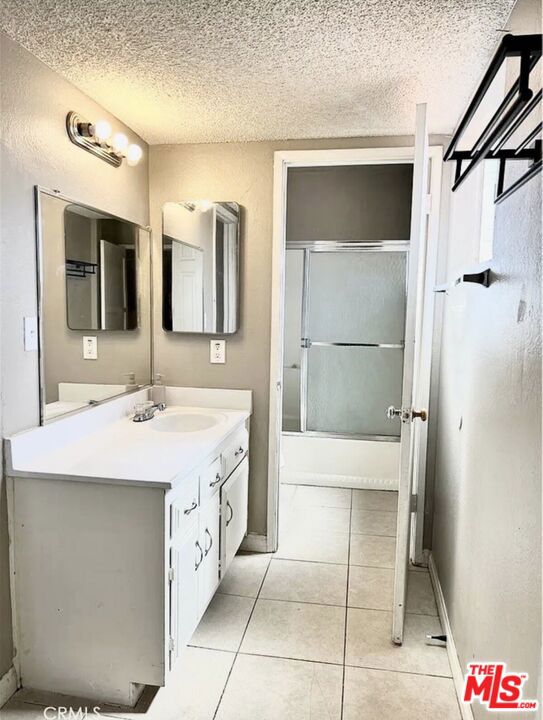 bathroom with vanity, combined bath / shower with glass door, a textured ceiling, and tile patterned floors