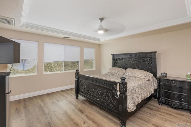 bedroom with black fridge, light hardwood / wood-style flooring, a tray ceiling, crown molding, and ceiling fan