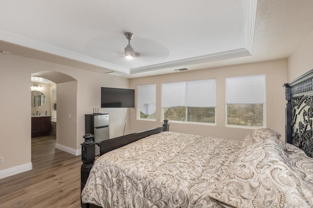 bedroom with ensuite bathroom, a tray ceiling, hardwood / wood-style floors, and ceiling fan