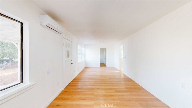 hallway with light hardwood / wood-style flooring, a wall unit AC, and a healthy amount of sunlight