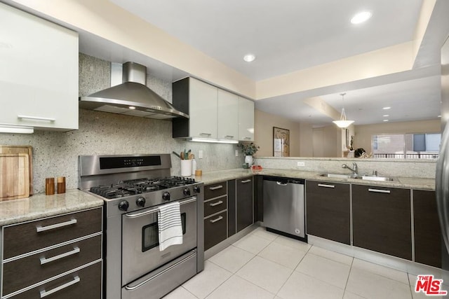 kitchen with stainless steel appliances, wall chimney range hood, backsplash, white cabinetry, and sink