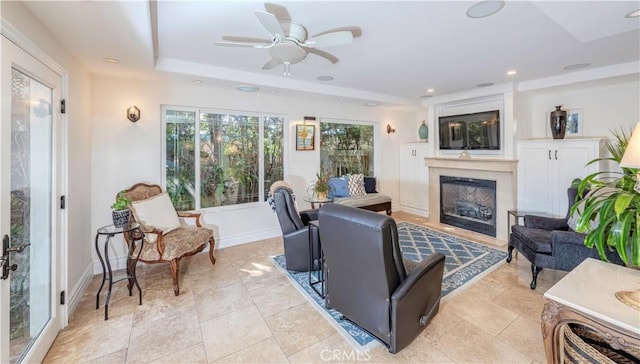 living room featuring a glass covered fireplace, baseboards, a tray ceiling, and recessed lighting