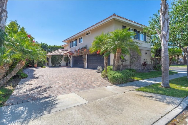 view of front facade with decorative driveway, a tile roof, an attached garage, and stucco siding