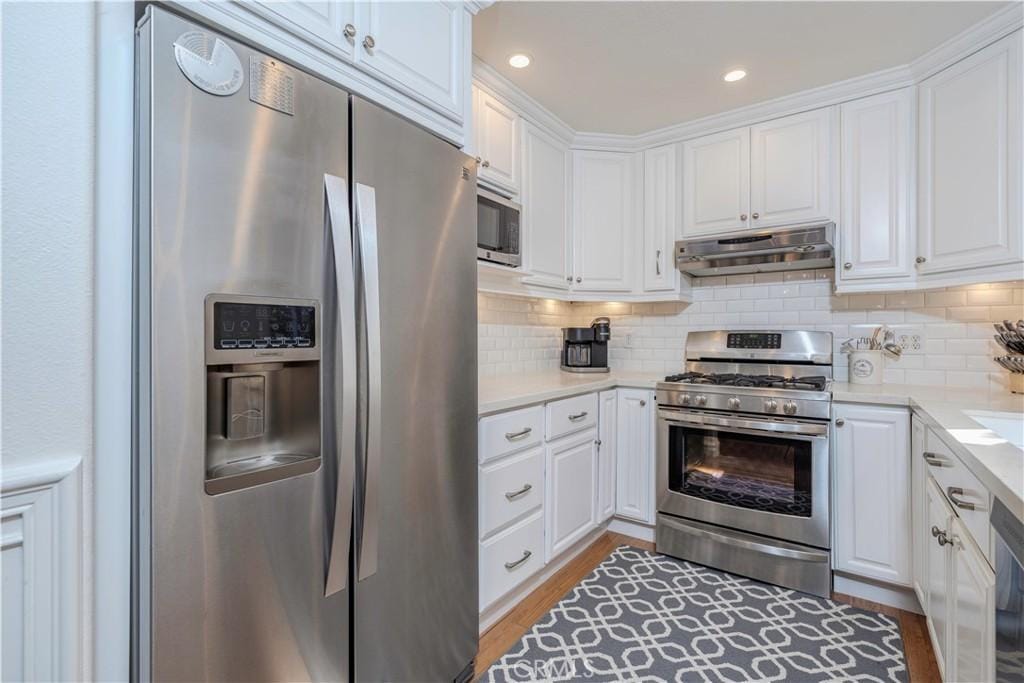 kitchen featuring stainless steel appliances, decorative backsplash, white cabinetry, and under cabinet range hood