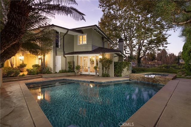 pool at dusk featuring an in ground hot tub and a patio area