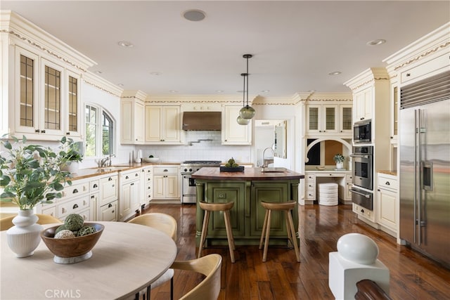 kitchen with dark wood-type flooring, a kitchen island with sink, built in appliances, and decorative light fixtures