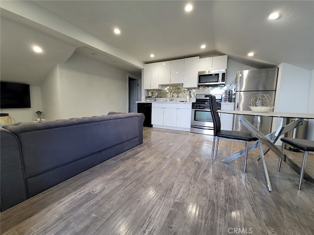 kitchen with tasteful backsplash, sink, hardwood / wood-style floors, white cabinetry, and stainless steel appliances