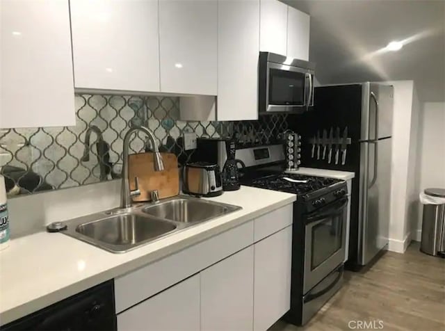 kitchen with tasteful backsplash, appliances with stainless steel finishes, sink, light hardwood / wood-style floors, and white cabinets