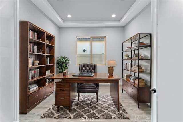 office featuring a tray ceiling and light hardwood / wood-style flooring