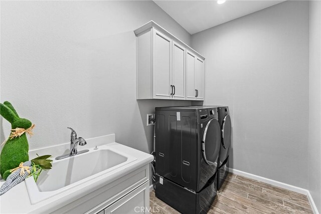 clothes washing area with cabinets, hardwood / wood-style floors, washer and clothes dryer, and sink