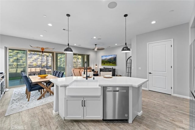 kitchen featuring dishwasher, a kitchen island with sink, sink, hanging light fixtures, and light hardwood / wood-style flooring