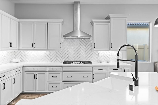 kitchen featuring wall chimney range hood, decorative backsplash, white cabinetry, and stainless steel gas stovetop