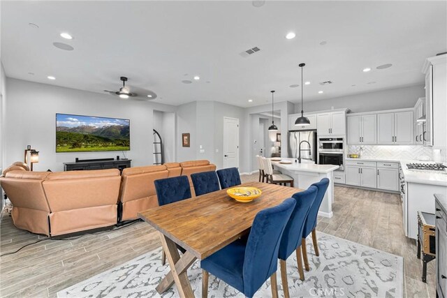 dining space featuring ceiling fan, sink, and light wood-type flooring