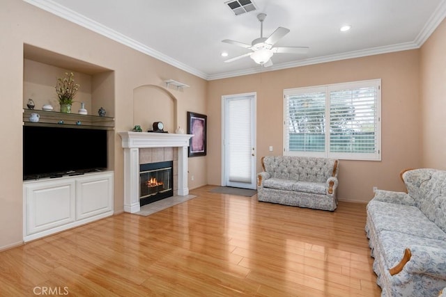 living room with a tile fireplace, crown molding, and light hardwood / wood-style floors