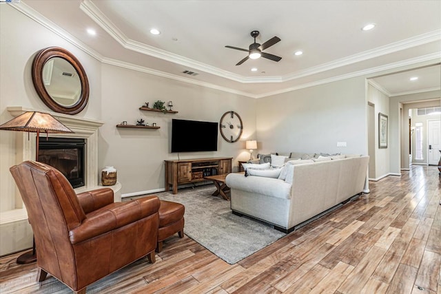 living room with ceiling fan, light hardwood / wood-style floors, a raised ceiling, and ornamental molding