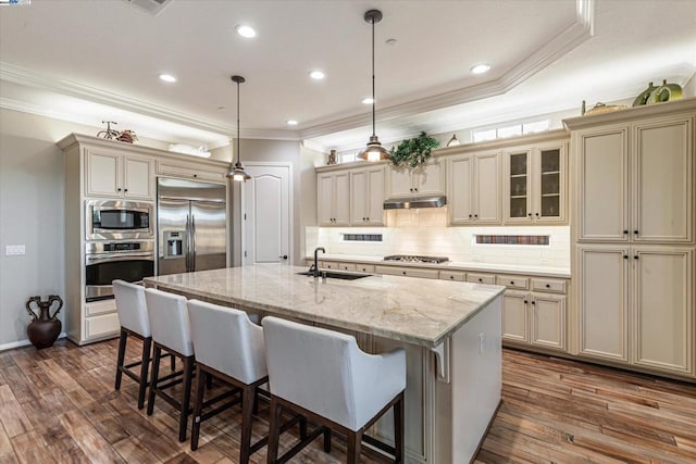 kitchen with dark wood-type flooring, sink, built in appliances, cream cabinetry, and an island with sink