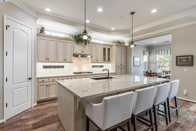 kitchen featuring light stone countertops, dark hardwood / wood-style flooring, a kitchen island with sink, cream cabinets, and hanging light fixtures