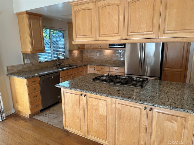 kitchen with tasteful backsplash, appliances with stainless steel finishes, sink, light wood-type flooring, and dark stone countertops