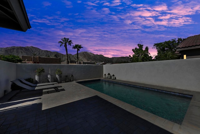 pool at dusk featuring a mountain view and a patio