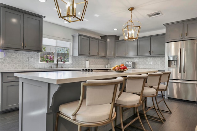 kitchen featuring tasteful backsplash, a kitchen island, pendant lighting, gray cabinetry, and stainless steel refrigerator with ice dispenser