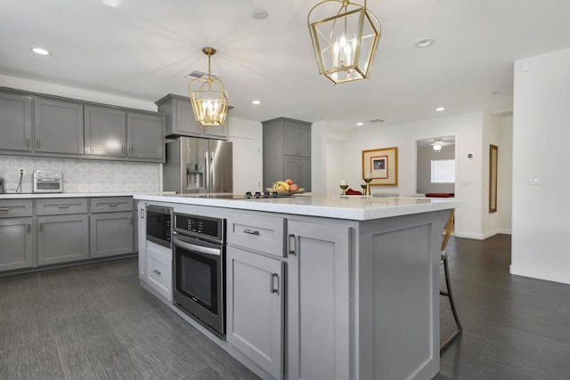 kitchen with hanging light fixtures, backsplash, appliances with stainless steel finishes, gray cabinets, and a center island